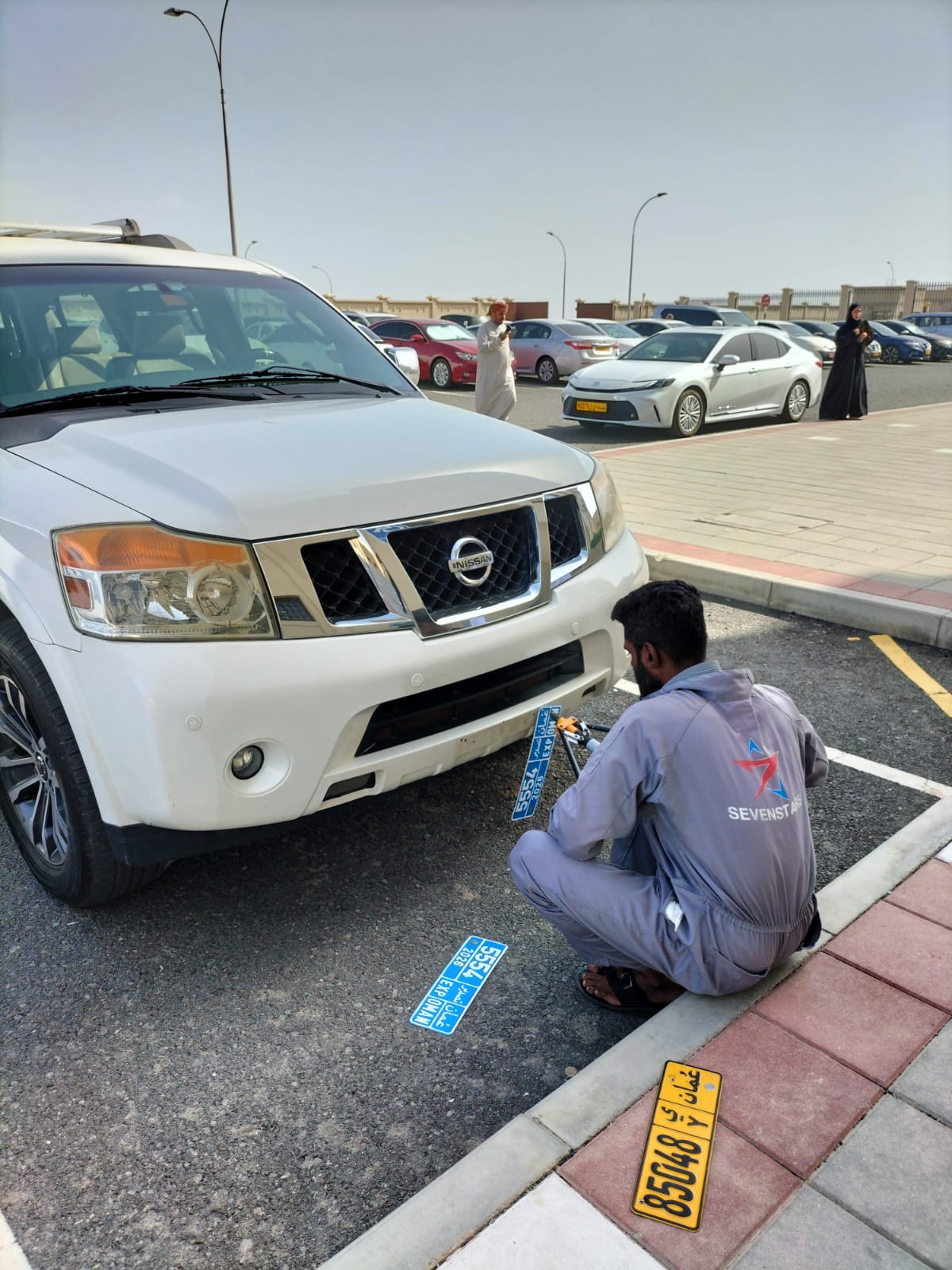 Mechanic fitting the blue EXP OMAN export number plates onto a Nissan Patrol in the ROP car park, Azaiba Muscat